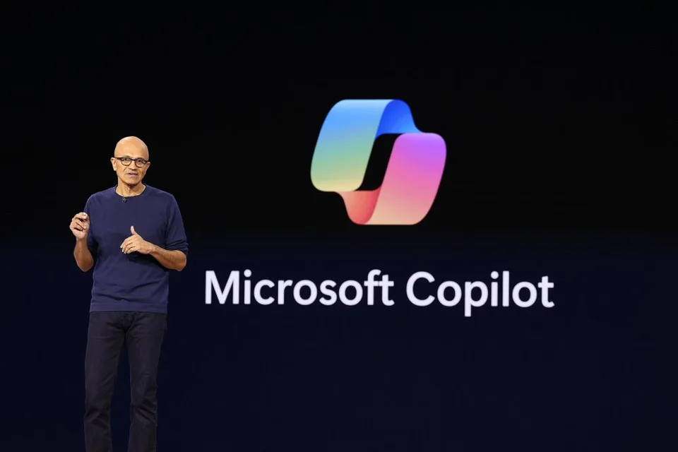 Microsoft CEO Satya Nadella standing beside a Microsoft Copilot display.