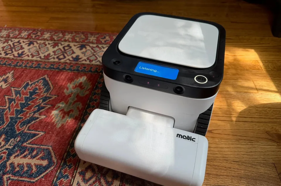 A Matic robot floor cleaner on a wooden floor beside a patterned rug.