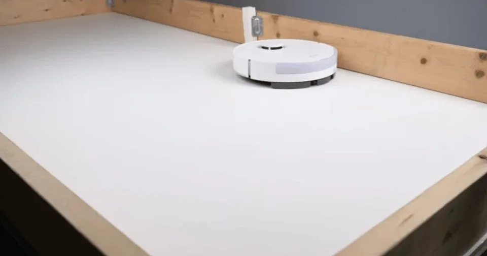 White Dreame robot vacuum and its docking station beside a carpeted test ramp in a Vacuum Wars studio.