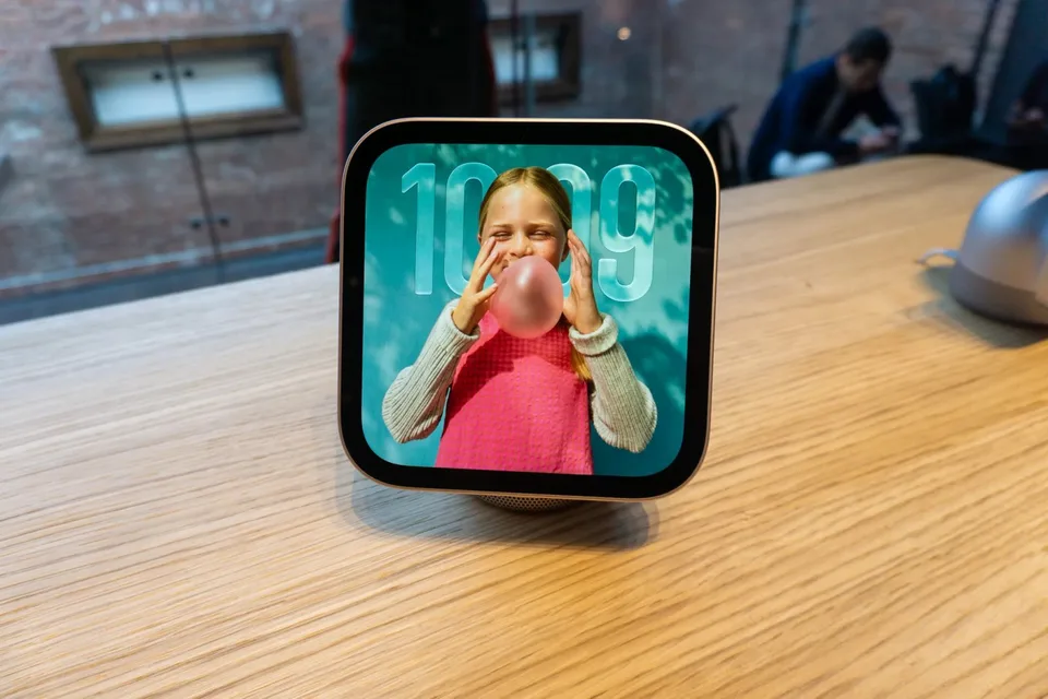 Two Apple smart-home displays on a wooden table, one showing a child and the other showing a clock face.