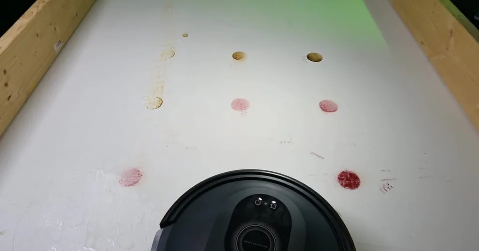 Robot vacuum testing area showing dried stains and wet puddles on a white floor surface.