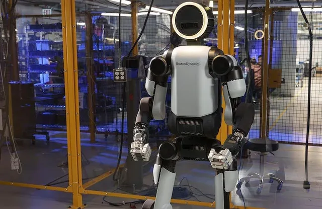 Humanoid robot standing inside a fenced industrial work area.