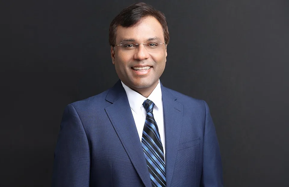 Rohit Prasad pictured beside a Boston Dynamics humanoid robot in an industrial workspace.