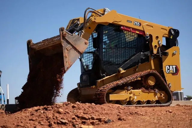 Caterpillar tracked loader tipping soil from its bucket at a construction site.