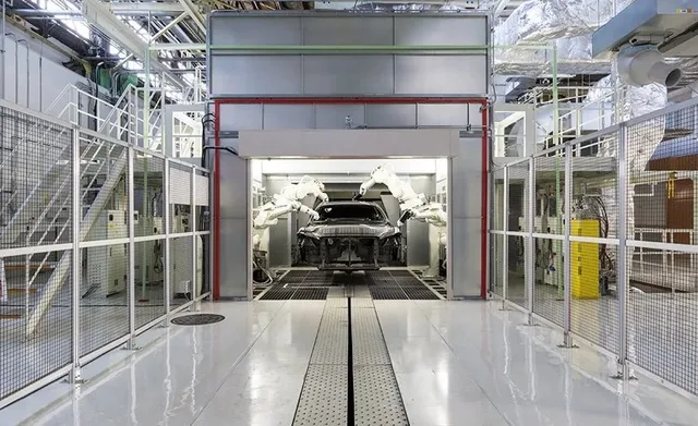 Automated vehicle assembly line inside a factory, with industrial robots working around a car body.