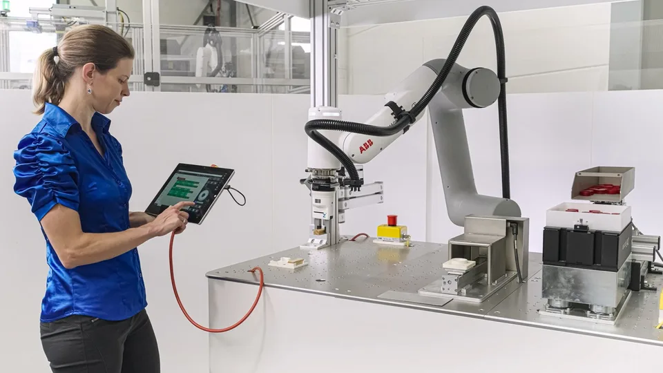 Operator uses a tablet beside an ABB industrial robot while another person holds a robot control device.