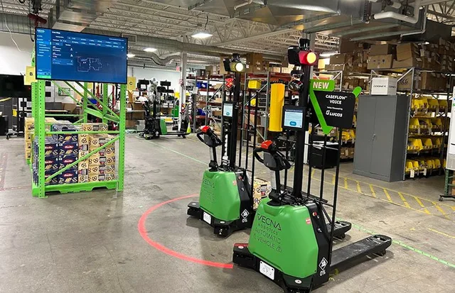Two autonomous mobile robots in a warehouse aisle beside storage racks and industrial equipment.